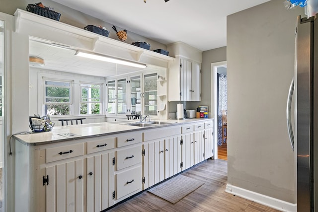 kitchen with baseboards, white cabinets, light countertops, light wood-type flooring, and a sink