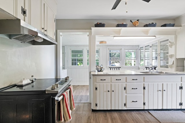 kitchen with white cabinets, light wood-style flooring, stainless steel electric stove, light countertops, and under cabinet range hood