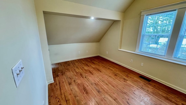 additional living space with a wealth of natural light, visible vents, vaulted ceiling, and wood finished floors