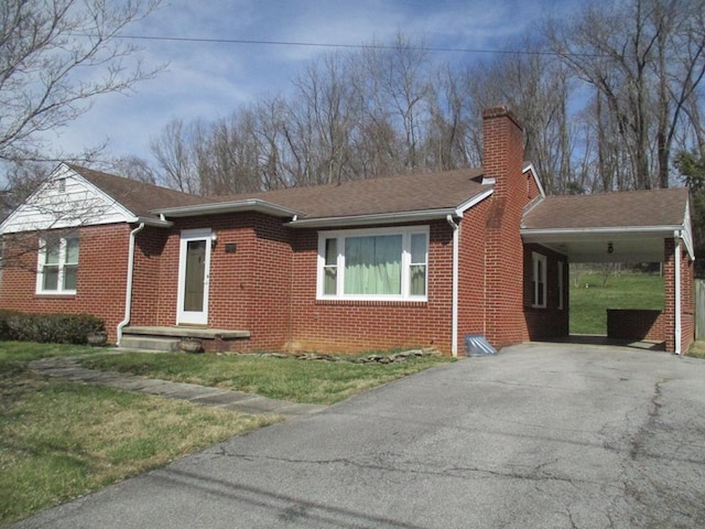 ranch-style home featuring driveway, a chimney, an attached carport, and brick siding