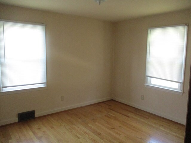 spare room with light wood finished floors, baseboards, and visible vents