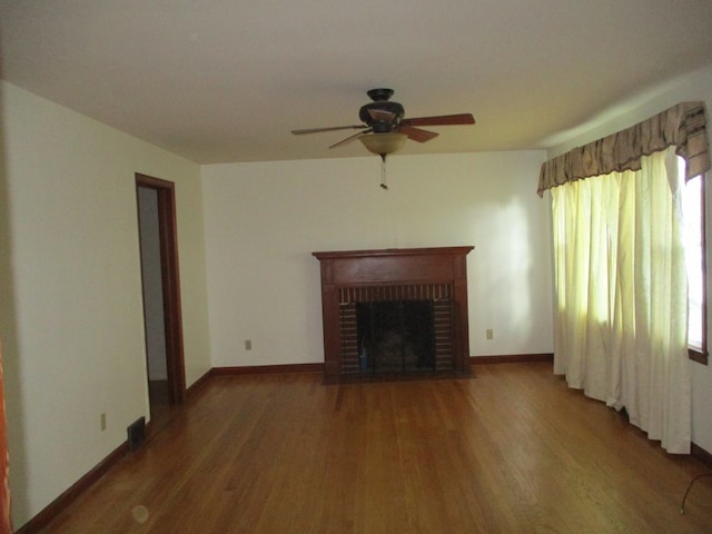 unfurnished living room with baseboards, wood finished floors, a ceiling fan, and a brick fireplace
