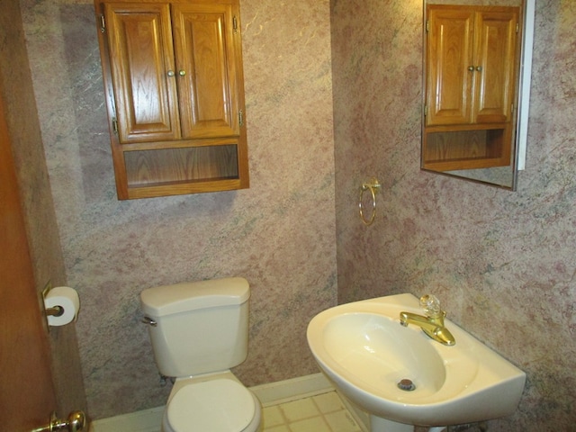 bathroom with wallpapered walls, a sink, toilet, and baseboards