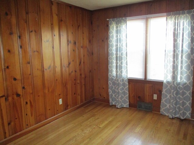 empty room featuring wooden walls, light wood-style floors, and visible vents