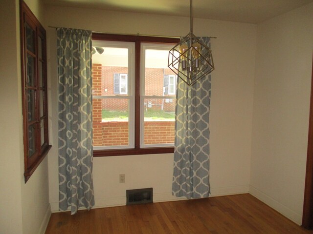 unfurnished dining area featuring baseboards, a notable chandelier, visible vents, and wood finished floors