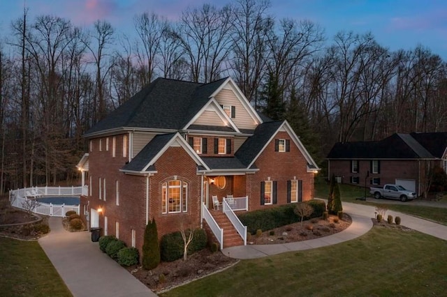 view of front of home with a porch, brick siding, stairs, driveway, and a front yard