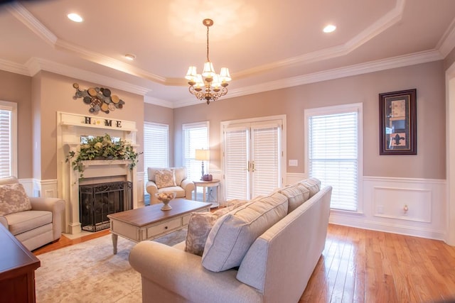 living area featuring a fireplace with flush hearth, wainscoting, a tray ceiling, light wood finished floors, and crown molding