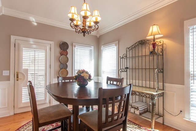 dining space with a notable chandelier, wainscoting, light wood-type flooring, and crown molding