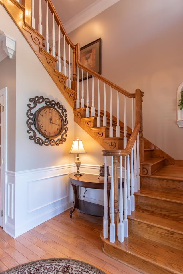 stairs with a decorative wall, wainscoting, wood finished floors, and crown molding