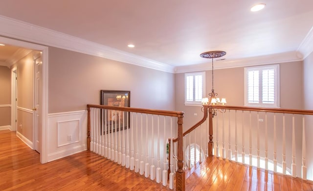 hall with wainscoting, ornamental molding, wood finished floors, an upstairs landing, and a notable chandelier