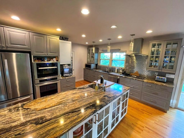 675 Pine Ridge Rd, Wytheville, VA 24382 - kitchen with stainless steel appliances, wall chimney range hood, light wood-style flooring, glass insert cabinets, and dark stone countertops