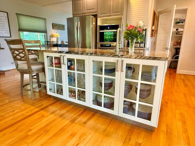 675 Pine Ridge Rd, Wytheville, VA 24382 - kitchen featuring appliances with stainless steel finishes, light wood-type flooring, dark stone counters, glass insert cabinets, and a center island with sink