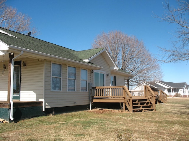 rear view of house with a wooden deck, roof with shingles, and a yard