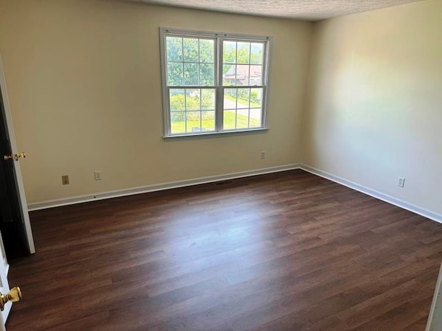 spare room with dark wood-style flooring, a textured ceiling, and baseboards