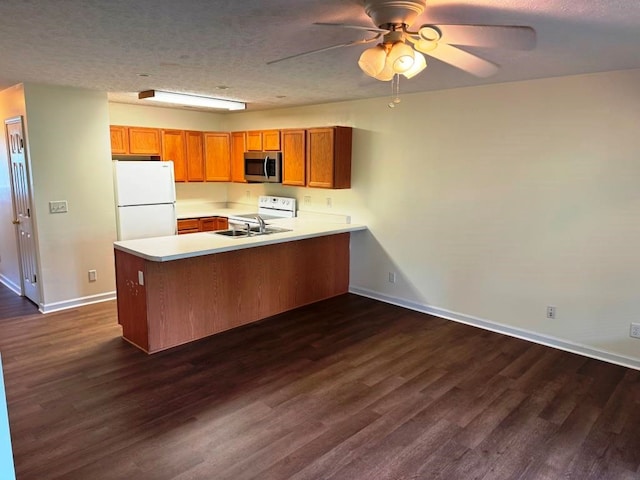 kitchen featuring light countertops, brown cabinetry, dark wood-type flooring, white appliances, and a peninsula