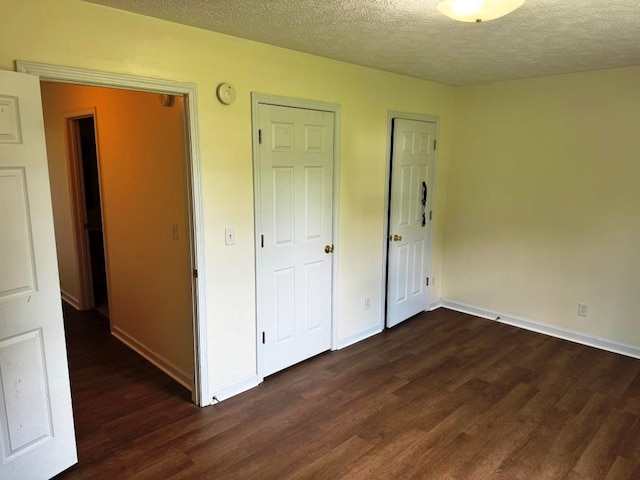 unfurnished bedroom featuring a textured ceiling, dark wood-style flooring, and baseboards