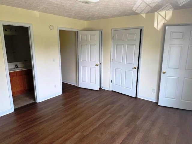 unfurnished bedroom with a textured ceiling, a sink, dark wood finished floors, baseboards, and ensuite bath