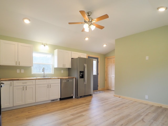 kitchen featuring vaulted ceiling, appliances with stainless steel finishes, sink, white cabinets, and light wood-type flooring