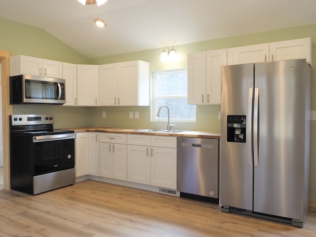 kitchen with lofted ceiling, sink, stainless steel appliances, and white cabinets