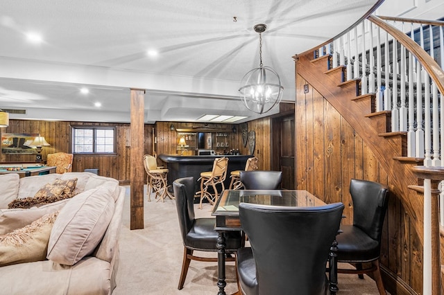 dining room with indoor bar, carpet flooring, an inviting chandelier, wood walls, and stairs