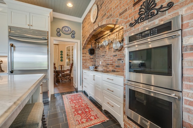 kitchen featuring white cabinets, appliances with stainless steel finishes, stone tile floors, and brick wall