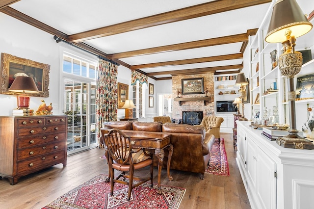living area with a brick fireplace, hardwood / wood-style floors, beam ceiling, and crown molding