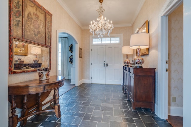 foyer featuring stone tile floors, ornamental molding, arched walkways, baseboards, and a notable chandelier