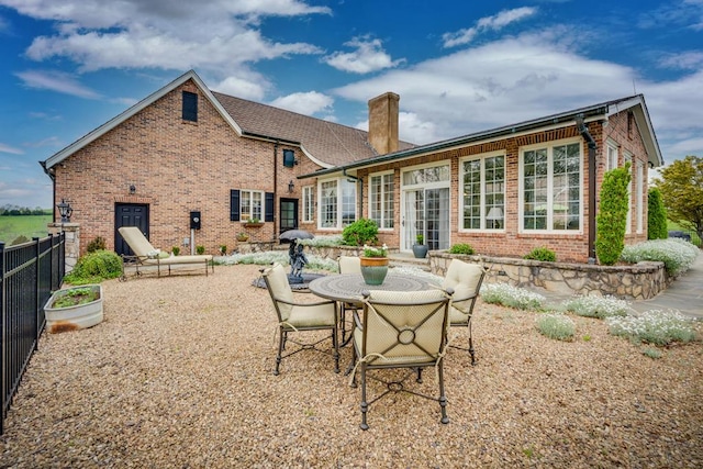 rear view of house featuring a chimney, outdoor dining area, fence, a patio, and brick siding