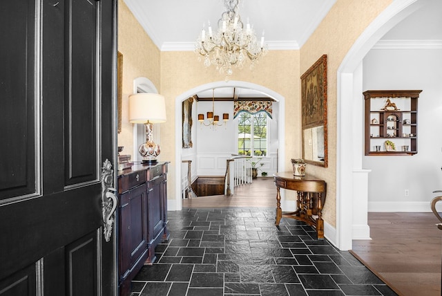 entrance foyer with stone tile flooring, arched walkways, a chandelier, and ornamental molding