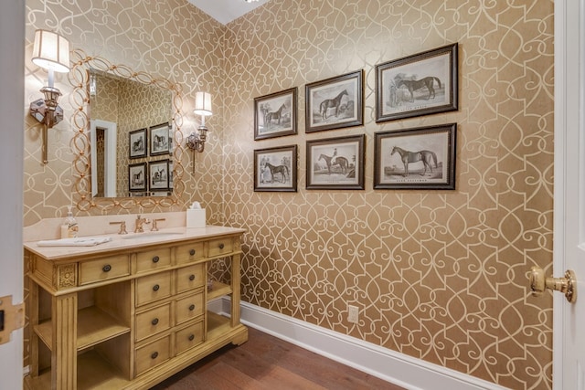 bathroom featuring baseboards, vanity, wood finished floors, and wallpapered walls