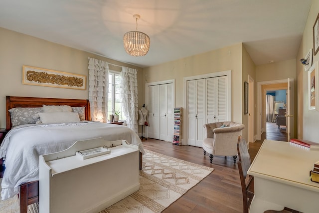 bedroom with a chandelier, wood finished floors, multiple closets, and baseboards