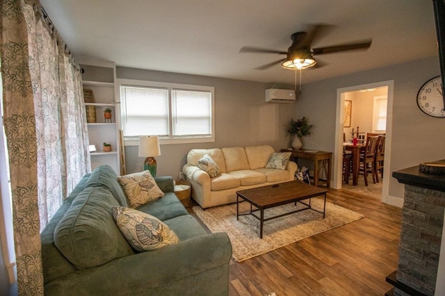 living room featuring ceiling fan, a wall unit AC, and light wood-type flooring