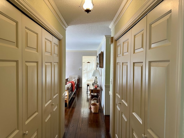 hall with dark wood-type flooring, ornamental molding, and a textured ceiling