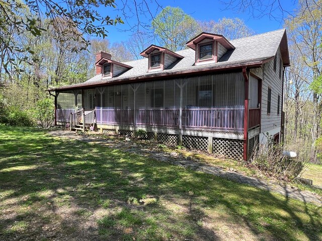 view of front of home with a front yard, a chimney, a shingled roof, and a sunroom