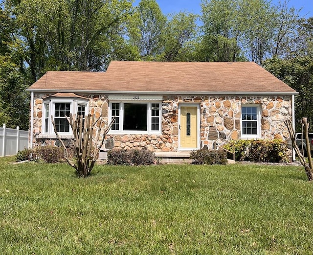view of front of property with a front yard, roof with shingles, stone siding, and fence