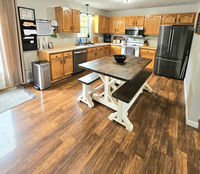 kitchen with dark wood finished floors, appliances with stainless steel finishes, a sink, light countertops, and baseboards