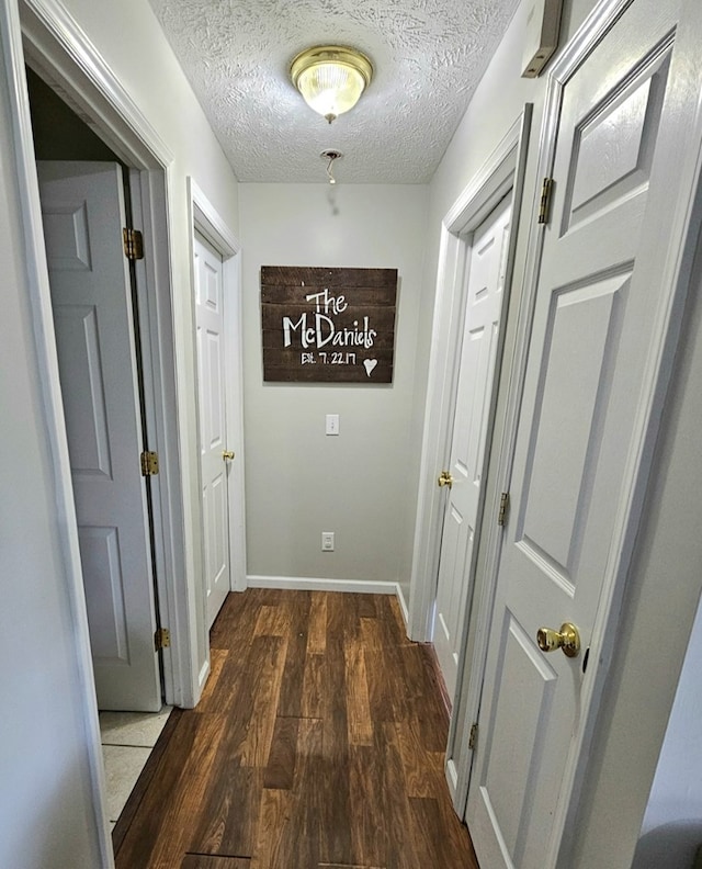 hall featuring a textured ceiling, baseboards, and wood finished floors