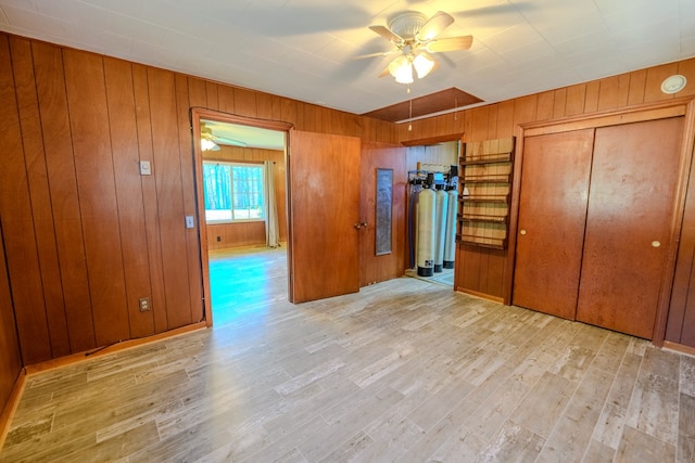 unfurnished bedroom featuring ceiling fan, wooden walls, and light wood-type flooring