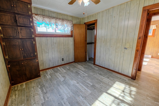 unfurnished bedroom featuring wood walls, ceiling fan, and light wood-type flooring