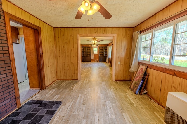 hallway featuring ornamental molding, a textured ceiling, light hardwood / wood-style floors, and wood walls