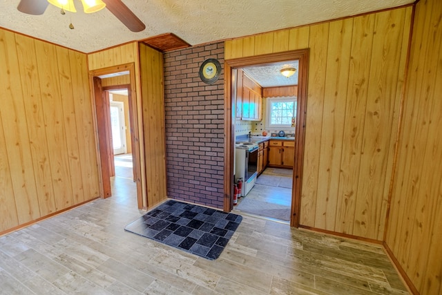 kitchen with light hardwood / wood-style flooring, a textured ceiling, wooden walls, electric stove, and ceiling fan