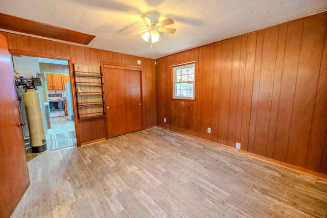 unfurnished bedroom featuring wood walls, ceiling fan, and light hardwood / wood-style flooring