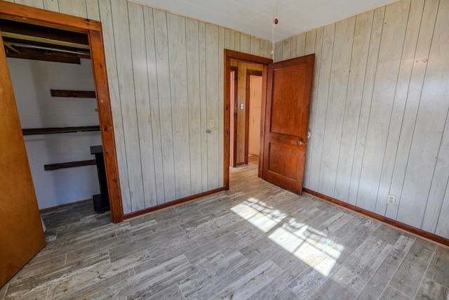 unfurnished bedroom with light hardwood / wood-style flooring, a closet, and wood walls