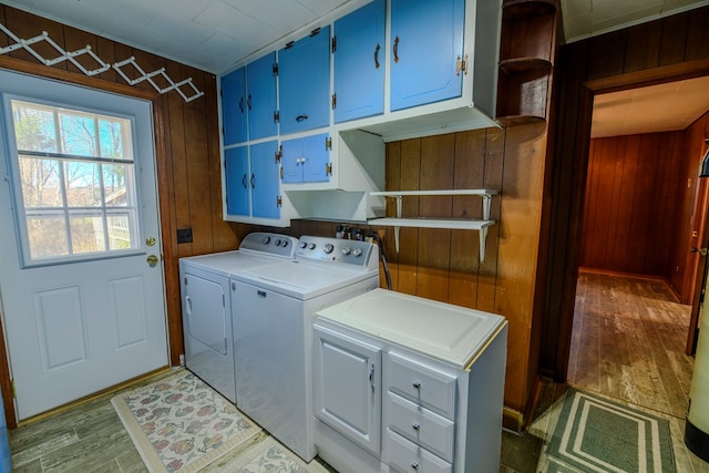 laundry area with washer and dryer, wooden walls, cabinets, and light hardwood / wood-style flooring