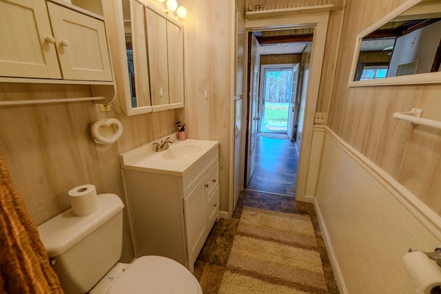 bathroom with vanity, wood walls, and toilet