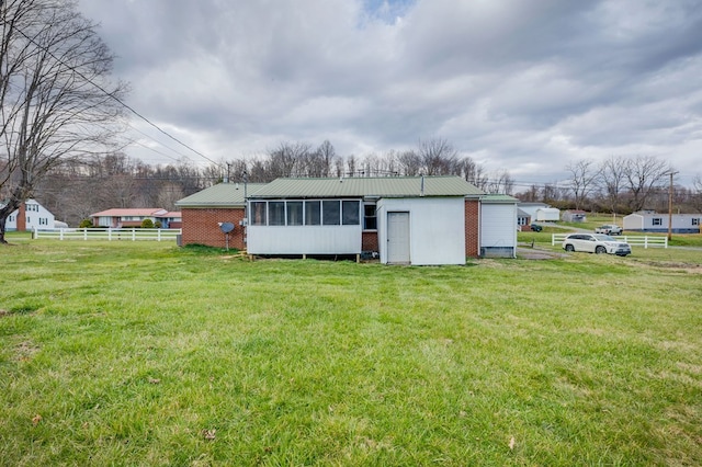 back of house featuring metal roof, a yard, a sunroom, and fence