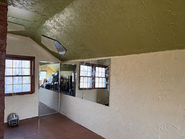 corridor with a textured ceiling, a textured wall, and vaulted ceiling