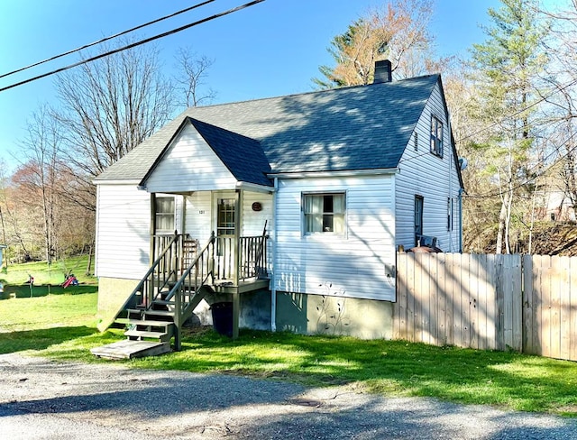 view of front of property featuring a front yard, roof with shingles, fence, and a chimney