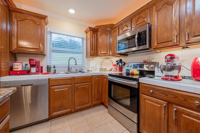 kitchen featuring appliances with stainless steel finishes, brown cabinetry, a sink, and tile counters