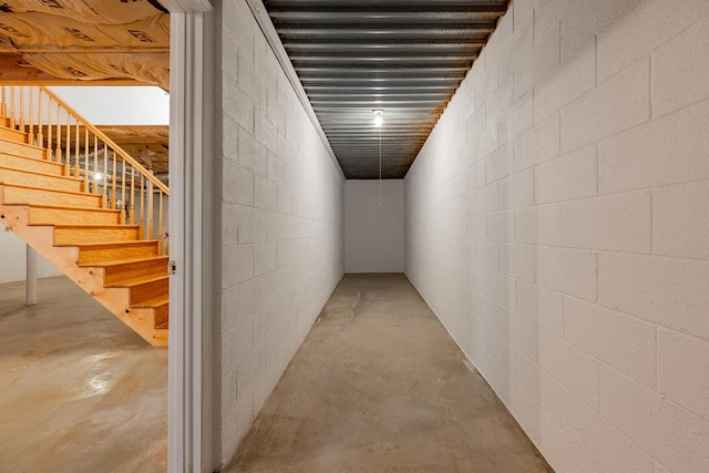 hall with concrete block wall, stairway, and concrete flooring